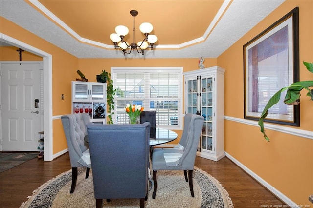 dining room with dark wood-type flooring, a raised ceiling, and a notable chandelier