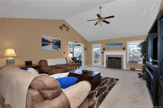 carpeted living room with a tiled fireplace, a textured ceiling, high vaulted ceiling, and ceiling fan