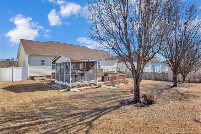 back of property with a wooden deck, a sunroom, and a lawn