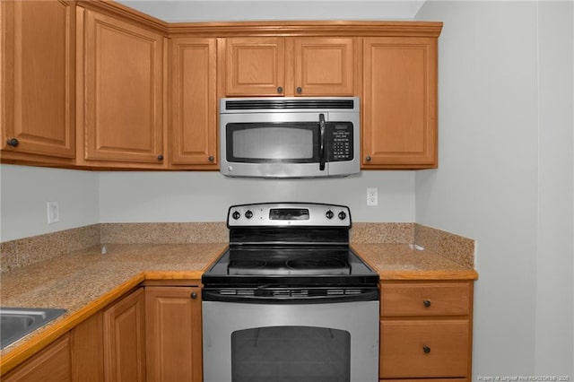 kitchen with appliances with stainless steel finishes, light stone countertops, and sink