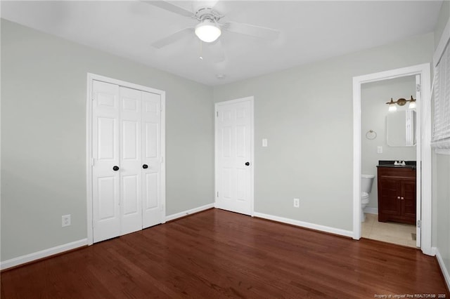 unfurnished bedroom featuring ceiling fan, dark hardwood / wood-style floors, ensuite bath, and a closet