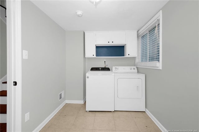 clothes washing area with cabinets, light tile patterned floors, and washer and clothes dryer