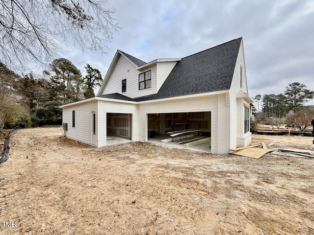 view of side of home with a garage and roof with shingles