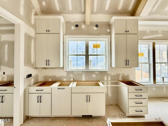 kitchen featuring beamed ceiling, plenty of natural light, and white cabinets