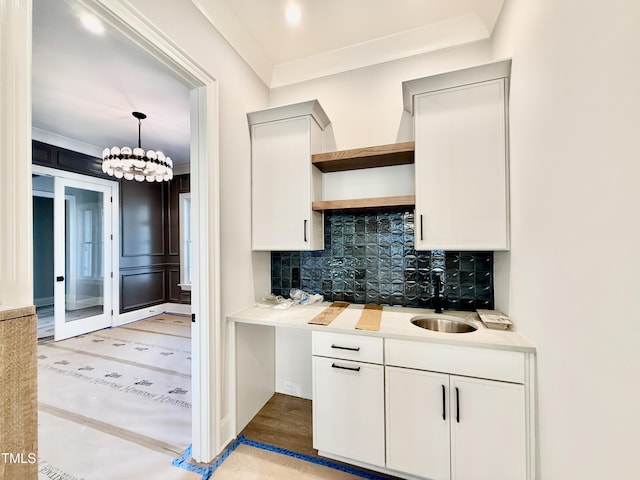 interior space with an inviting chandelier, a sink, light wood-style floors, decorative backsplash, and indoor wet bar