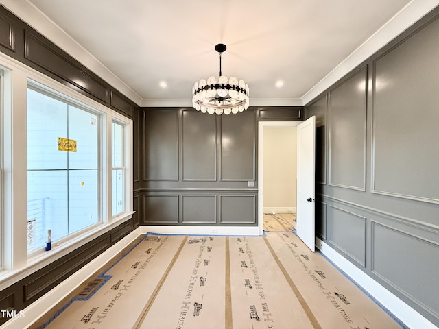 unfurnished dining area with a notable chandelier, a decorative wall, ornamental molding, and recessed lighting