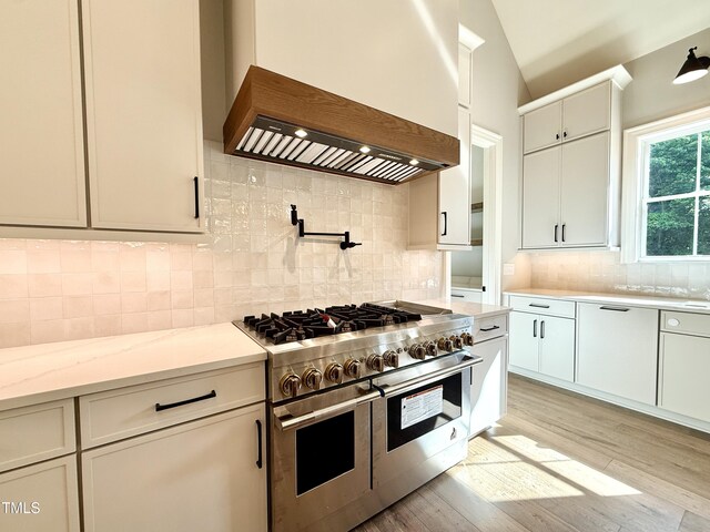5820 Shawood Dr, Raleigh, NC 27609 - kitchen featuring range with two ovens, premium range hood, light wood-style flooring, tasteful backsplash, and vaulted ceiling