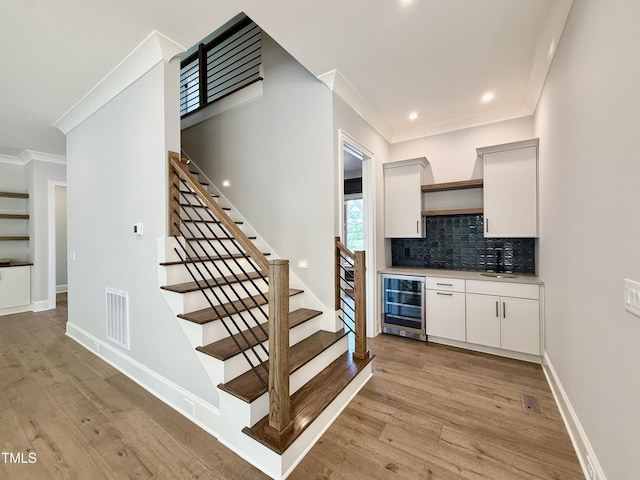 5820 Shawood Dr, Raleigh, NC 27609 - indoor bar with beverage cooler, ornamental molding, stairway, light wood-style flooring, and backsplash