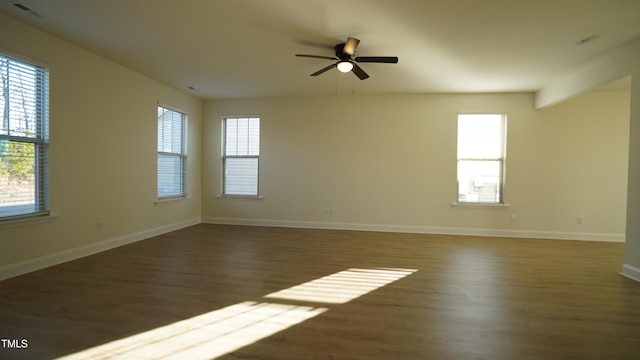 empty room featuring ceiling fan, dark wood-type flooring, and a healthy amount of sunlight