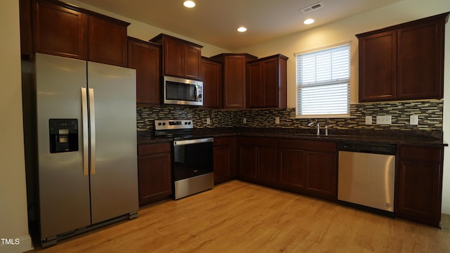 kitchen with tasteful backsplash, appliances with stainless steel finishes, sink, and light hardwood / wood-style flooring