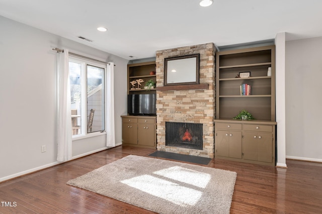 unfurnished living room featuring dark wood-type flooring, a stone fireplace, and built in features