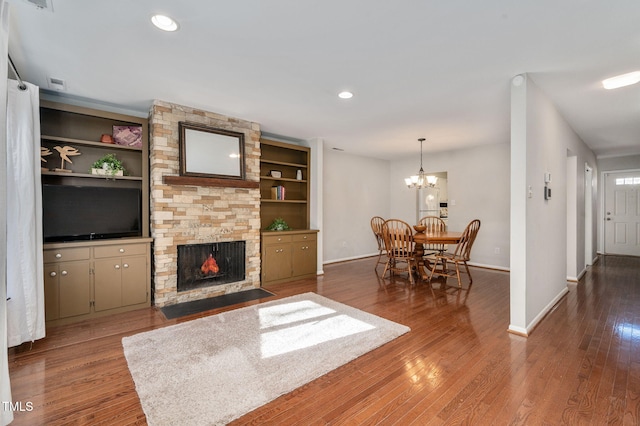 living room featuring a notable chandelier, a stone fireplace, wood-type flooring, and built in features