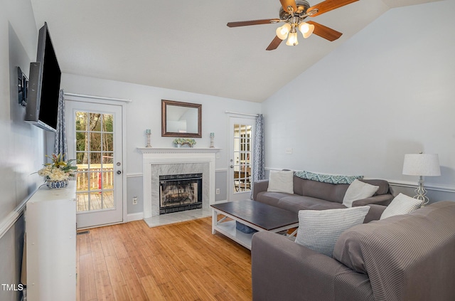 living room with ceiling fan, high vaulted ceiling, light wood-type flooring, and a high end fireplace