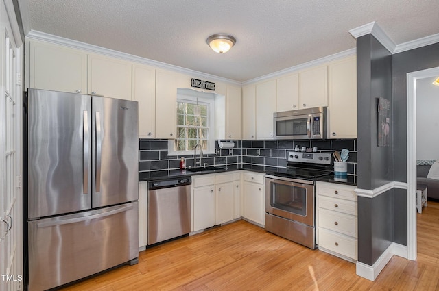 kitchen featuring appliances with stainless steel finishes, sink, white cabinets, ornamental molding, and light hardwood / wood-style flooring