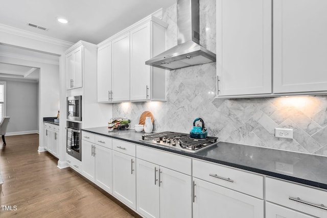 kitchen featuring wall chimney range hood, crown molding, appliances with stainless steel finishes, white cabinetry, and wood-type flooring