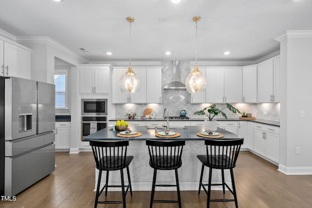 kitchen featuring wall chimney exhaust hood, appliances with stainless steel finishes, a center island with sink, and pendant lighting