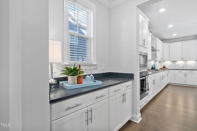 kitchen with dark wood-type flooring, white cabinetry, crown molding, tasteful backsplash, and stainless steel appliances