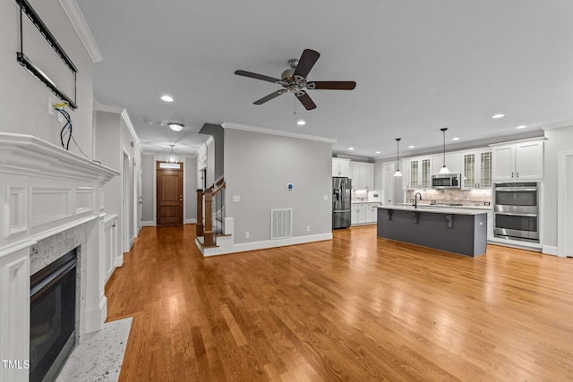 unfurnished living room featuring crown molding, sink, ceiling fan, and light hardwood / wood-style floors