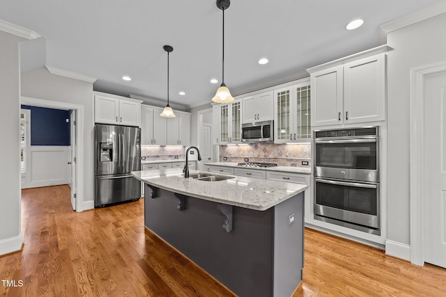 kitchen with an island with sink, white cabinetry, sink, light stone counters, and stainless steel appliances