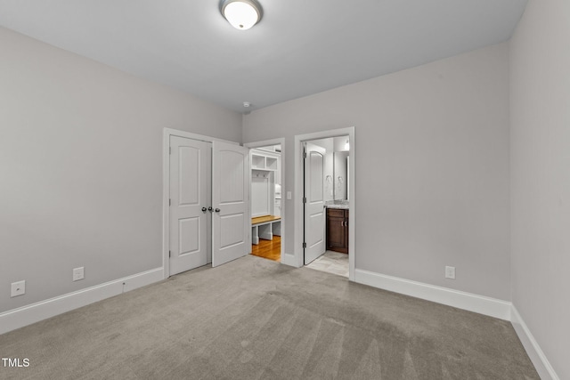 unfurnished bedroom with light colored carpet, a closet, and ensuite bath