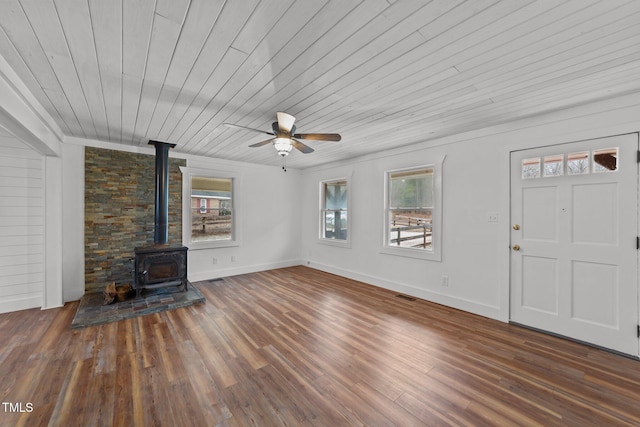 unfurnished living room featuring dark wood-type flooring, a wealth of natural light, wooden ceiling, and a wood stove