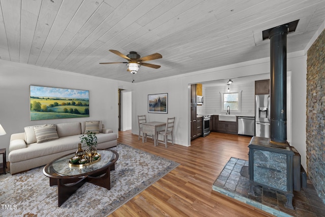 living room featuring sink, wood ceiling, a wood stove, hardwood / wood-style flooring, and ceiling fan