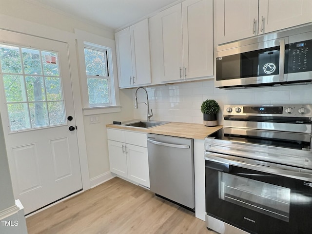 kitchen with sink, appliances with stainless steel finishes, butcher block counters, backsplash, and white cabinets