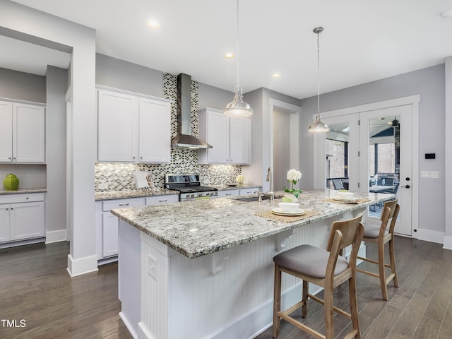 kitchen with a sink, decorative backsplash, stainless steel range, a kitchen breakfast bar, and wall chimney range hood