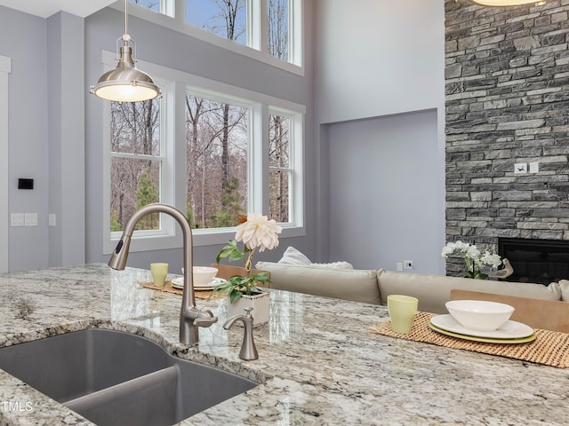 kitchen featuring pendant lighting, a sink, light stone counters, a high ceiling, and a fireplace