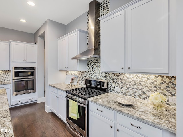 kitchen with wall chimney range hood, dark wood finished floors, decorative backsplash, stainless steel appliances, and white cabinetry