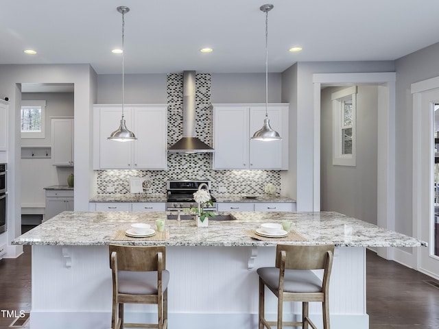 kitchen featuring dark wood-type flooring, a sink, appliances with stainless steel finishes, white cabinets, and wall chimney range hood