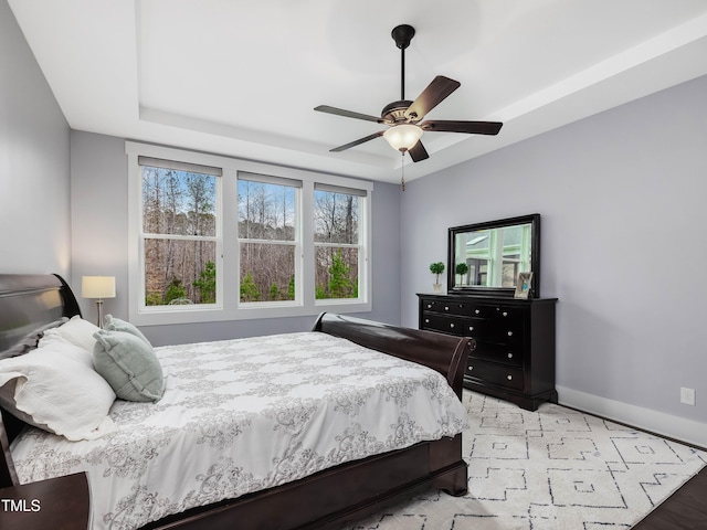 bedroom featuring a ceiling fan, a tray ceiling, and baseboards