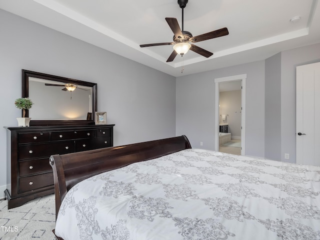 bedroom featuring ensuite bath, a raised ceiling, and a ceiling fan