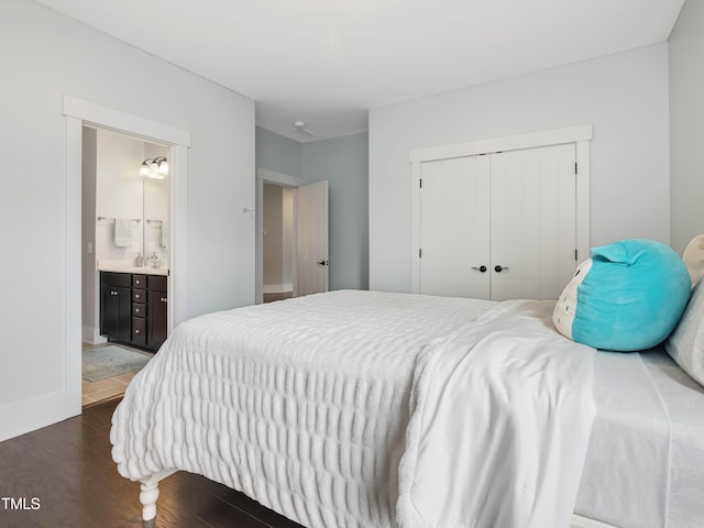 bedroom featuring wood finished floors, baseboards, ensuite bath, a sink, and a closet