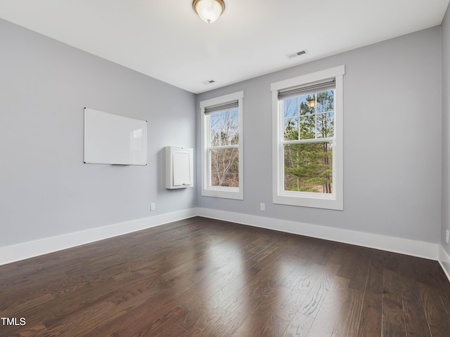 empty room featuring dark wood-type flooring, visible vents, and baseboards