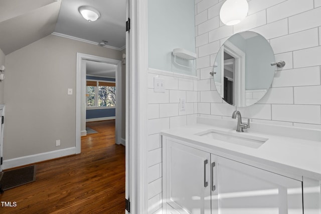 bathroom featuring lofted ceiling, vanity, ornamental molding, hardwood / wood-style flooring, and backsplash