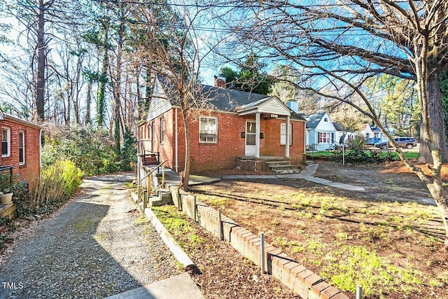 bungalow featuring brick siding, a chimney, and driveway