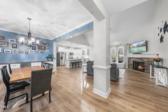 dining area featuring a stone fireplace, light wood finished floors, an inviting chandelier, and baseboards