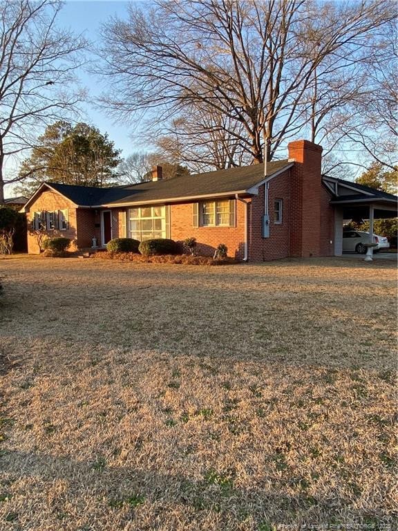 700 W 20th St W, Lumberton, NC 28358 - view of side of home featuring a carport, a yard, brick siding, and a chimney