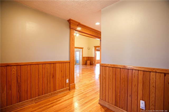 corridor with wooden walls, light hardwood / wood-style floors, and a textured ceiling