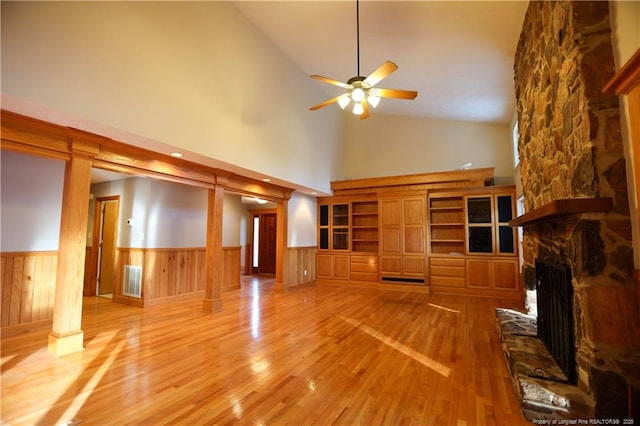 unfurnished living room with ceiling fan, high vaulted ceiling, a fireplace, wood-type flooring, and ornate columns