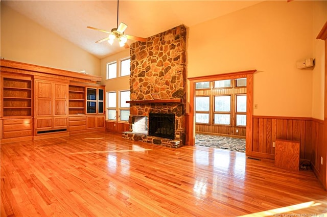 unfurnished living room featuring ceiling fan, wood-type flooring, a stone fireplace, and high vaulted ceiling