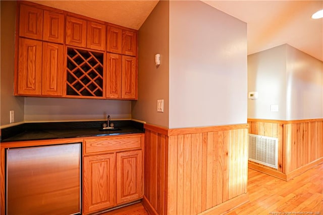 kitchen featuring sink, refrigerator, light wood-type flooring, kitchen peninsula, and wood walls