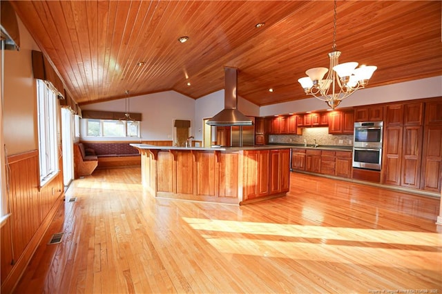 kitchen with pendant lighting, range hood, a notable chandelier, vaulted ceiling, and stainless steel double oven