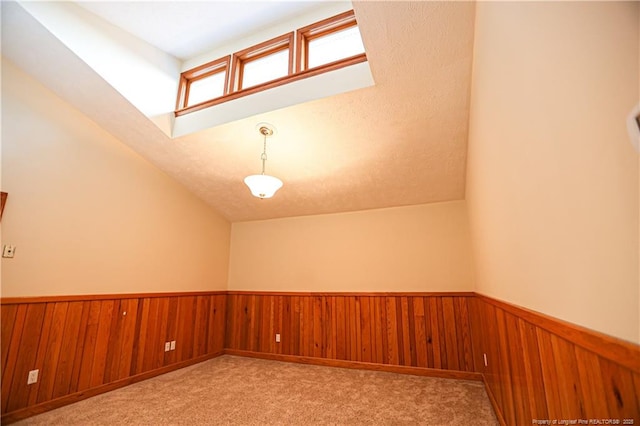 carpeted empty room featuring vaulted ceiling and wood walls