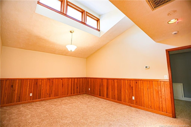 carpeted empty room with lofted ceiling, wooden walls, and a textured ceiling