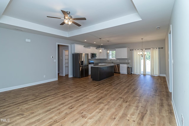 kitchen featuring a kitchen island, appliances with stainless steel finishes, decorative light fixtures, white cabinets, and a raised ceiling