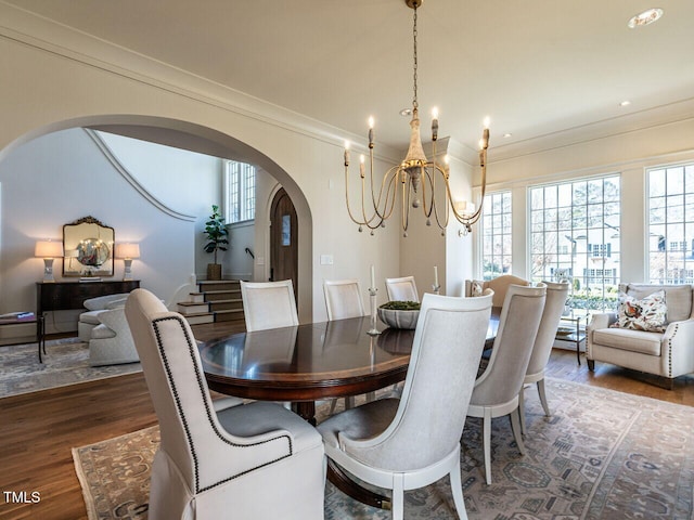 dining room with ornamental molding, arched walkways, an inviting chandelier, and wood finished floors