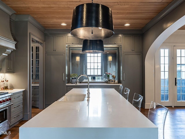 kitchen featuring arched walkways, a sink, gray cabinets, and wood ceiling