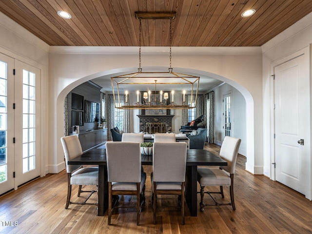 dining area with arched walkways, ornamental molding, wooden ceiling, and wood finished floors